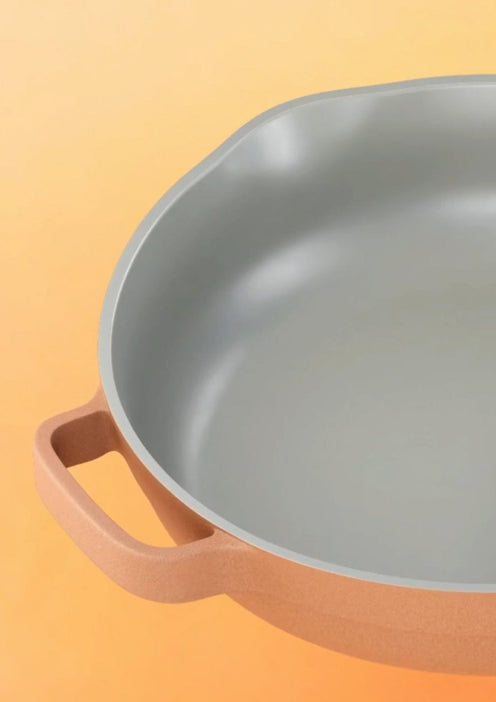 A close-up of a gray nonstick skillet with a light brown handle, set against a gradient orange background.