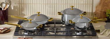 Set of silver cookware with gold handles on a stove
