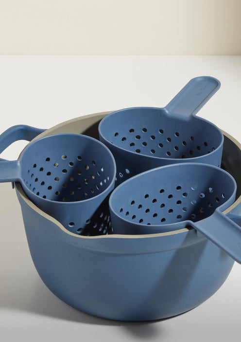 A set of three blue plastic colanders with handles are nested inside a matching blue mixing bowl on a white surface.