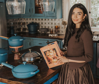 our place founder shiza shahid in kitchen with blue cookware and our place cookbook
