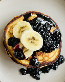 Stack of pancakes with blueberry sauce and banana slices on a white plate