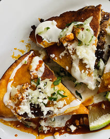 Birria Quesadillas with sour cream, cheese, and lime on a white plate