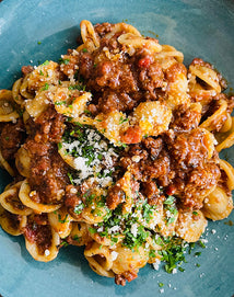 Pasta dish with meat sauce and herbs on a blue plate