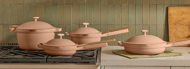 Set of pink cookware on a stove with a tiled wall background