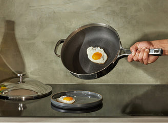Person holding a frying pan with a fried egg on a kitchen counter.