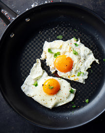 Two fried eggs with green herbs on a black frying pan