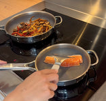 Person cooking salmon and vegetables on a stovetop