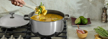 Person cooking in a kitchen with a pot on the stove, surrounded by ingredients.