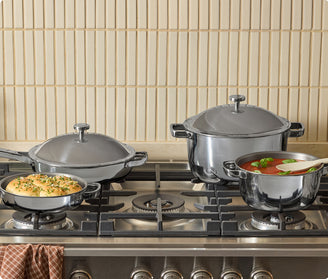 Set of titanium cookware on a gas stove with a tiled wall background