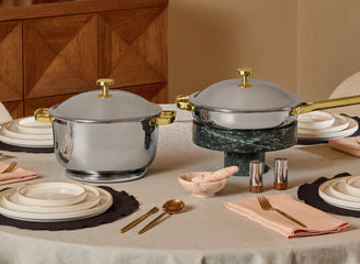 Silver covered dishes with gold handles on a table with tableware and decor.