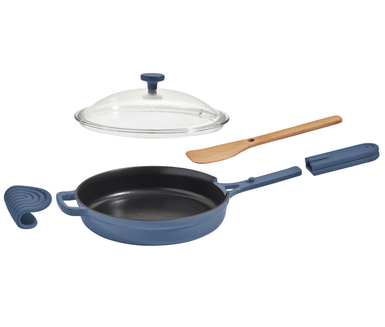 A blue cast iron skillet with a matching handle cover, a glass lid, a wooden spatula, and a silicone handle grip set against a white background.