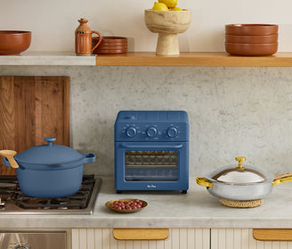 Blue oven on a kitchen counter with a pot and fruit bowl in a home setting