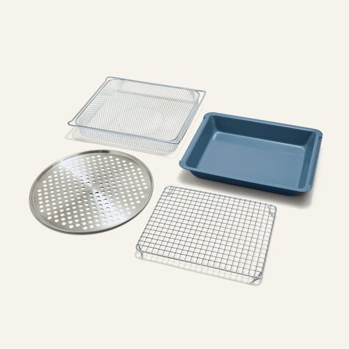 The Wonder Oven Pro Chef’s Kit features a blue rectangular pan, square mesh basket, round perforated tray, and square wire rack on a plain background.