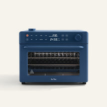The Wonder Oven Pro is a blue mini oven with a digital display, buttons, two wire racks, and air fryer functionality, shown on a plain white background.