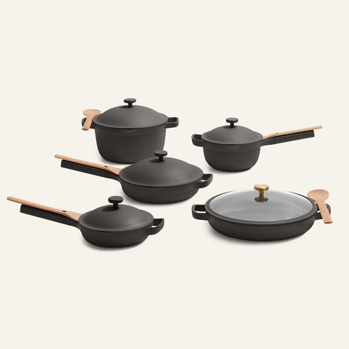 The Cookware Set + Dual Handle Always Pan, including five black ceramic pieces with wooden handles and two utensils, is displayed on a light background.
