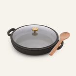 The Ceramic Nonstick Dual Handle Always Pan 32 cm is black, round, nonstick, with two handles, a glass lid with gold knob, and comes with a wooden spoon.