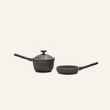 The Tiny Cookware Duo—a black, non-toxic saucepan with lid and matching frying pan, both with long handles—is set against a plain light background, evoking the style of the Always Pan.