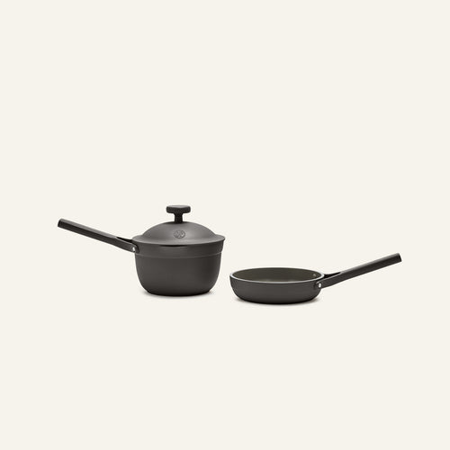 The Tiny Cookware Duo—a black, non-toxic saucepan with lid and matching frying pan, both with long handles—is set against a plain light background, evoking the style of the Always Pan.