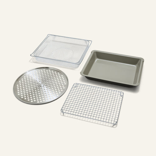 The Wonder Oven Pro Chef’s Kit includes a mesh basket, rectangular pan, round perforated tray, and wire cooling rack on a white background.