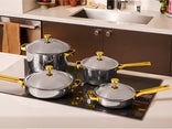 Set of titanium cookware with gold handles on a kitchen stove.
