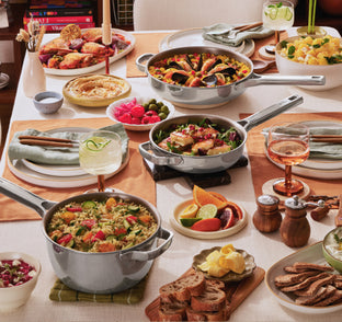 Dining table set with various dishes including pots, plates, and glasses on a checkered tablecloth.