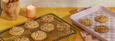 Cookies on a cooling rack and baking sheet with a candle on a kitchen counter.
