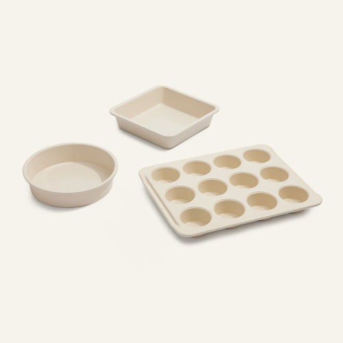 A beige Wonder Oven Pro Baker’s Kit featuring PFAS-free nonstick pans—muffin tin, square cake pan, and round cake pan—set against a plain background.