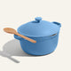 The Ceramic Nonstick Perfect Pot 6 L, in family size, features a matching blue lid and handles, and comes with a wooden spoon resting on the side, all displayed against a plain light background.