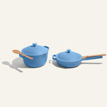 The Cookware Duo—featuring a blue pot with lid and spoon, plus a pan with lid and wooden handle—rests on a light background, making an ideal addition to your 18-piece cookware set.