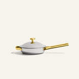 A silver-colored Titanium Always Pan Pro 20 cm (2.0) frying pan with a lid, gold-toned handle, and gold-toned lid knob.