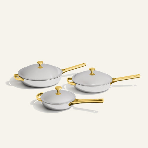 Titanium Pro Always Pan Trio (2.0) featuring three stainless steel pans of varying sizes with gold-toned handles and lids.