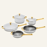 Titanium Pro Cookware Set+ featuring five stainless steel pieces with gold-toned handles and lids, including two lidded pots, two frying pans, and a deep skillet.