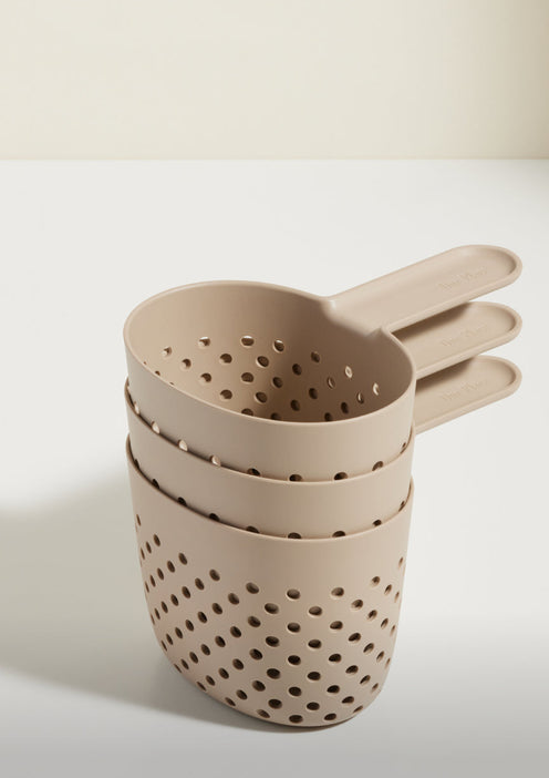 Three beige plastic colanders with handles are nested together on a white surface against a light background.
