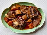 Slow-cooked beef and vegetable dish on a green plate with a white background