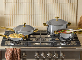 Set of titanium cookware on a gas stove with a tiled backsplash.