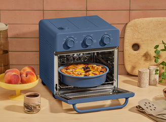 Blue toaster oven with a pie inside on a kitchen counter.