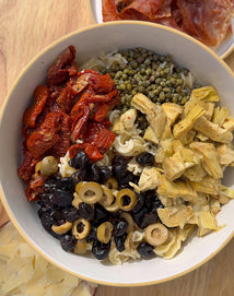 Assorted dried pasta and vegetables in a white bowl on a wooden surface