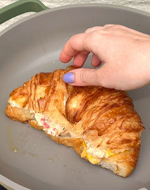 Hand holding a croissant with a crab filling on a green frying pan