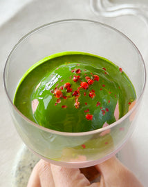 matcha  dessert with strawberry toppings in a clear glass held by a hand.