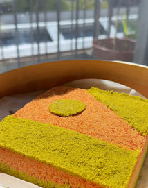 Colorful layered cake with green, orange, and yellow layers on a wooden tray.