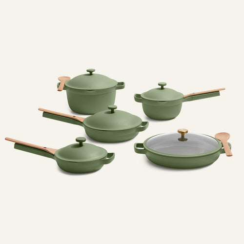 Five green Cookware Set + Dual Handle Always Pan pieces with light wooden handles, nonstick pans, and a glass lid are arranged on a plain background.