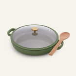The Ceramic Nonstick Dual Handle Always Pan 32 cm in green with a glass lid (gold knob) and wooden spoon, arranged on a plain light background.