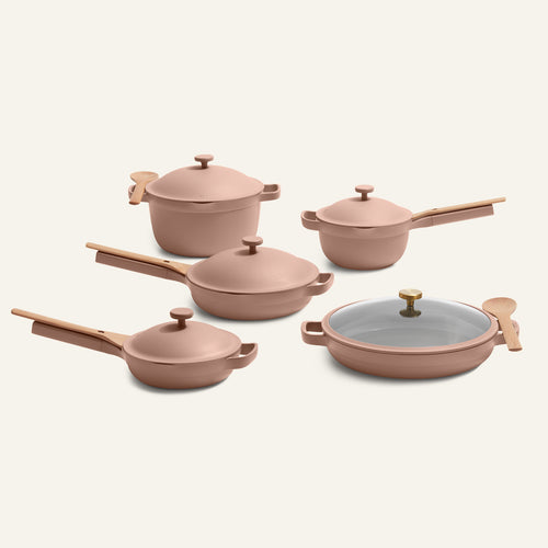 The Cookware Set + Dual Handle Always Pan includes five pink nonstick pieces with wooden handles, lidded pots and pans, and a wooden spoon, all on a plain background.