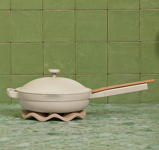 Beige ceramic pot with wooden handle on a green tiled background