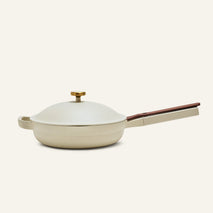 The Always Pan 2.0 in beige, part of a bestselling cookware line, features a matching domed lid, gold knob, brown main handle, and helper handle, displayed on a plain light background.