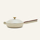 The Always Pan 2.0 in beige, part of a bestselling cookware line, features a matching domed lid, gold knob, brown main handle, and helper handle, displayed on a plain light background.